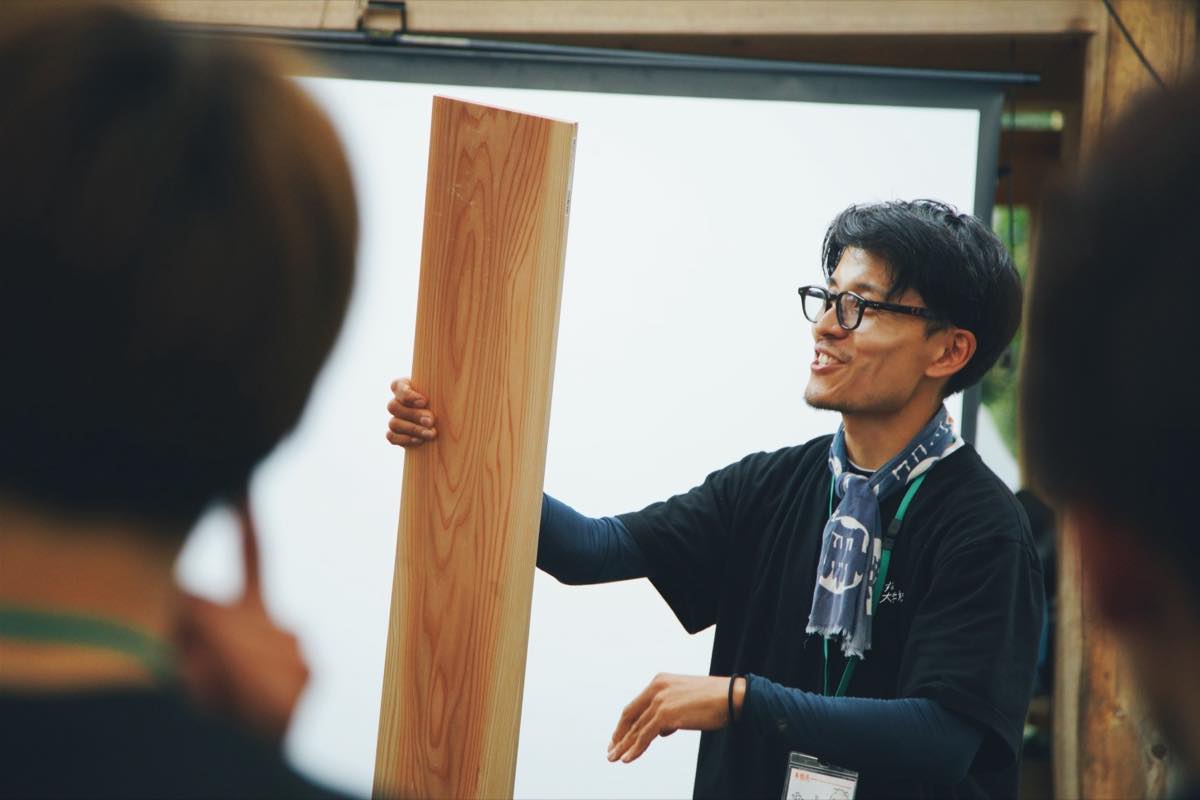 木材を手に、参加者へ説明する尾井田将年